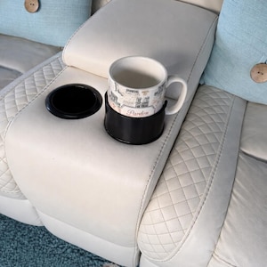 May include: Cream-colored leather sofa with a built-in cup holder and a mug. The mug has a decorative design and the word "Pardon" printed on it. Light blue throw pillows with wooden button accents are also visible.