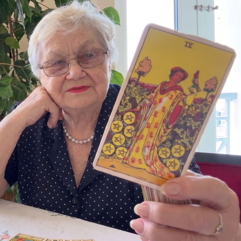 Puede incluir: Una carta de tarot rectangular que muestra el Nueve de Oros, con una figura vestida con una t&uacute;nica amarilla adornada con s&iacute;mbolos rojos, de pie en un jard&iacute;n con nueve monedas de oro, con el n&uacute;mero romano IX impreso en la parte superior central.