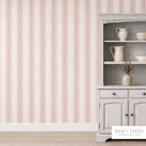 Puede incluir: Una habitación con papel pintado a rayas rosas y blancas y un armario gris. El armario tiene estantes con jarras y cuencos blancos. Un jarrón con flores secas está en el estante inferior. El texto "SAM + THEO" es visible.