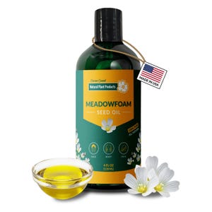 Puede incluir: Una botella verde de aceite de semilla de Meadowfoam con tapa negra, un pequeño cuenco de aceite y flores blancas. La etiqueta dice "Natural Plant Products" y "100% Pure All Natural". Una etiqueta con la bandera estadounidense dice "Made in USA". La botella contiene 118 ml.