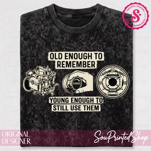 Może przedstawiać: Czarna i szara koszulka z napisem "OLD ENOUGH TO REMEMBER, YOUNG ENOUGH TO STILL USE THEM." Projekt zawiera ilustracje gaźnika, dłoni trzymającej ssanie i bębna hamulcowego.