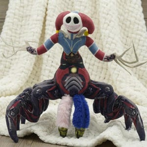 May include: A plush doll featuring a white skull-like head with a wide grin and red jester-style hat. The torso is blue and red, with long, thin, pale arms. The lower body has multiple dark, segmented legs and two fuzzy legs in pink and blue.
