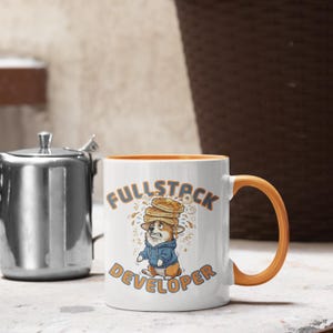 May include: White ceramic mug with an orange handle and interior. The mug features a cartoon corgi wearing a blue hoodie and a stack of pancakes on its head. The words "FULLSTACK DEVELOPER" are printed on the mug.