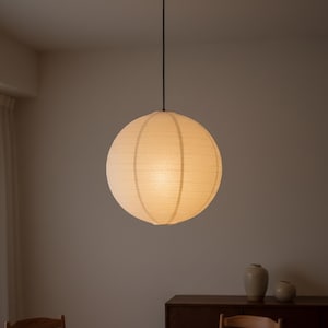 Könnte beinhalten: Eine runde, cremefarbene Pendelleuchte. Das Licht ist kugelförmig, mit vertikalen Streifen und einem weichen, diffusen Schein. Es hängt an einem schwarzen Kabel und erzeugt eine warme, einladende Atmosphäre. Die Leuchte ist ein modernes Design.