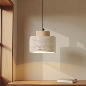 Könnte beinhalten: Eine zylindrische Pendelleuchte mit hellbeigem Steinschirm und Holzaufsatz. Das Licht hängt an einem braunen Kabel. Die Leuchte ist von innen beleuchtet und erzeugt einen warmen Schein.