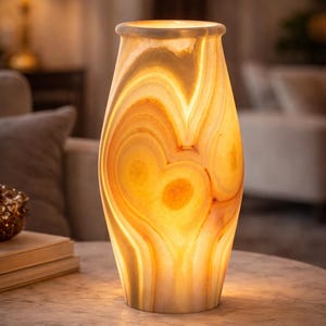 Può includere: Lampada decorativa in onice, che emana un caldo bagliore ambrato. La lampada presenta un motivo a spirale unico nei toni dell'arancione e del crema. È posizionata su un tavolo con piano in marmo e base in metallo dorato. Un elemento decorativo per la casa.