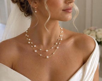 May include: A double-strand gold chain necklace featuring evenly spaced white pearls, paired with matching single pearl drop earrings. The jewelry is worn with a white off-the-shoulder satin garment and a sheer veil.