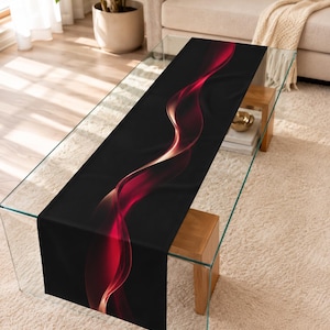 May include: A rectangular table runner featuring a solid black background with a central, flowing abstract design of vibrant red and soft orange light waves that curve and twist along the length of the fabric in a smooth, continuous motion.
