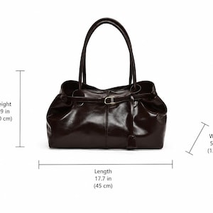 May include: A dark brown handbag with two top handles and a central strap featuring a metallic buckle. The bag measures 7.9 inches in height, 5.1 inches in width, and 17.7 inches in length, as indicated by the visible dimension labels.