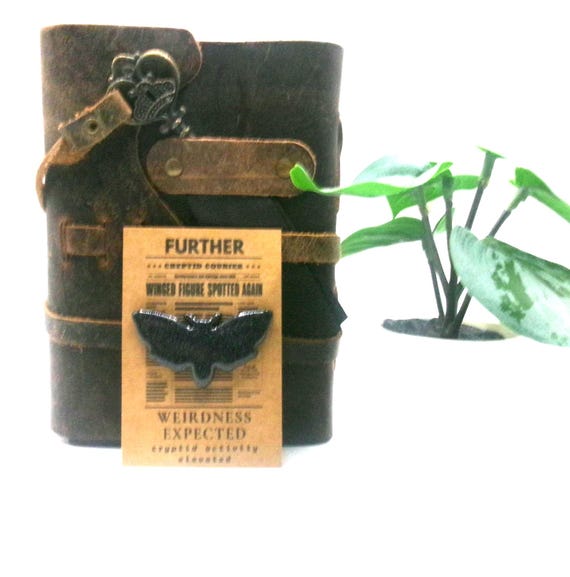 A handmade Mothman charm card from a "Cryptid Courier Collection" — niche, nerdy, and genuinely delightful for anyone who unironically loves cryptid lore.