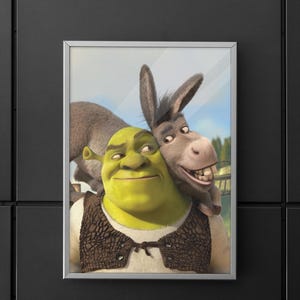 Puede incluir: Impresión enmarcada que presenta a Shrek, un ogro verde, y a Asno, un burro gris, sonriendo. Shrek lleva un chaleco marrón sobre una camisa blanca. El fondo muestra un cielo azul y follaje verde.