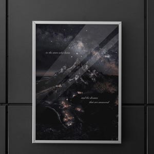Könnte beinhalten: Ein gerahmter Druck mit einer Berglandschaft unter einem Sternenhimmel. Das Kunstwerk hat einen silbernen Rahmen und enthält den Text "to the stars who listen" und "and the dreams that are answered". Die Farbpalette ist überwiegend dunkel.