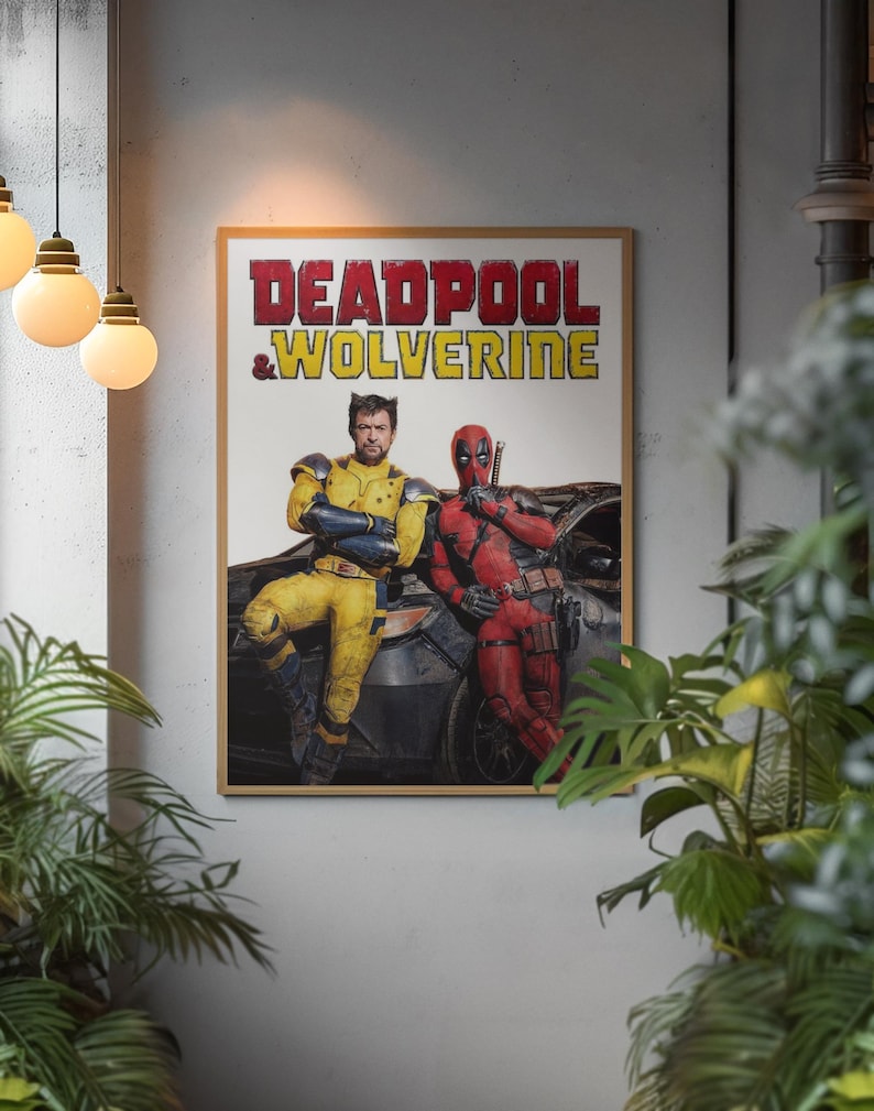Puede incluir: Un p&oacute;ster enmarcado con los personajes Deadpool y Wolverine. El texto del t&iacute;tulo es rojo y amarillo. Wolverine lleva un traje amarillo y azul, y Deadpool un traje rojo. El p&oacute;ster se muestra en una pared gris.