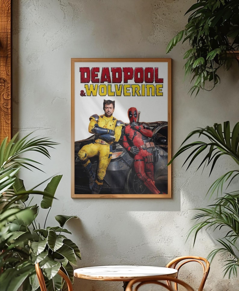 Puede incluir: Un p&oacute;ster enmarcado con el texto "DEADPOOL & WOLVERINE" en rojo y amarillo. La imagen muestra dos personajes disfrazados, uno de amarillo y otro de rojo, apoyados en un coche. El p&oacute;ster est&aacute; en un marco de madera, sobre una pared gris.