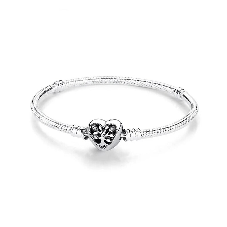 May include: A silver snake chain bracelet featuring a heart-shaped charm in the center. The charm displays an intricate tree of life design with small embedded clear stones. The bracelet includes two fixed stations along the chain for charm placement.