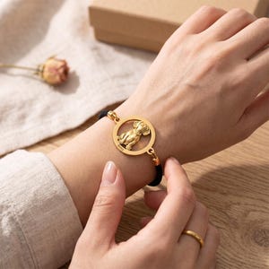 Peut inclure: Un bracelet à breloque circulaire doré présentant une découpe de chien au centre avec le nom Bailey gravé sur le bord inférieur. La breloque est fixée à un bracelet en cordon noir fin qui s'enroule autour du poignet pour un ajustement sûr.