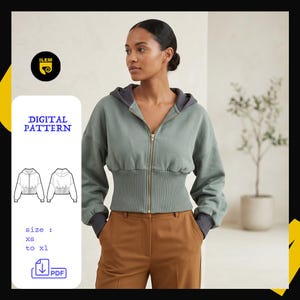 May include: A sage green zip-up hoodie with a wide ribbed waistband and dark gray cuffs. The garment features a front zipper closure and a hood. A digital pattern file is available for sizes XS to XL, indicated by text and a line drawing illustration.