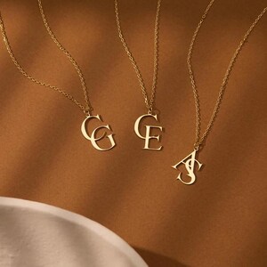 May include: Three gold-toned necklaces, each featuring a pendant with two overlapping capital letters. The pendants display the letter combinations CG, CE, and AS. Each necklace consists of a delicate gold-colored chain attached to the metal letters.