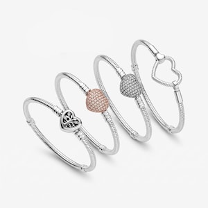 May include: Four silver-tone snake chain bracelets arranged in a row. The first features a heart-shaped charm with a tree design, the second a rose gold-tone pav&eacute; heart, the third a silver-tone pav&eacute; heart, and the fourth a plain heart-shaped clasp.