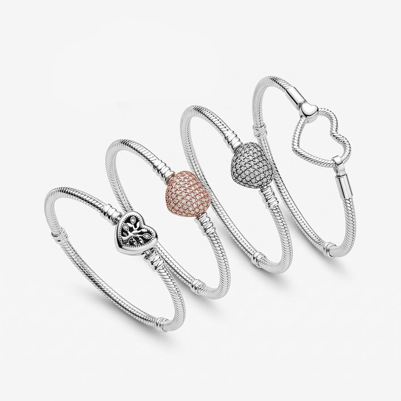 May include: Four silver-tone snake chain bracelets arranged in a row. The first features a heart-shaped charm with a tree design, the second a rose gold-tone pav&eacute; heart, the third a silver-tone pav&eacute; heart, and the fourth a plain heart-shaped clasp.
