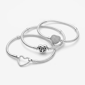 Peut inclure: Trois bracelets en chaîne serpent argentée. L'un présente un fermoir en forme de cœur avec un motif d'arbre, un autre un fermoir en forme de cœur pavé de petites pierres claires, et le troisième un fermoir en forme de cœur ouvert. Argent poli.