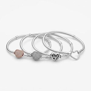 May include: Four silver-toned snake chain bracelets featuring heart-shaped charms. One charm is rose gold-toned with pav&eacute; stones, one is silver-toned with pav&eacute; stones, one is a silver heart with a tree motif, and one is a simple open heart clasp.