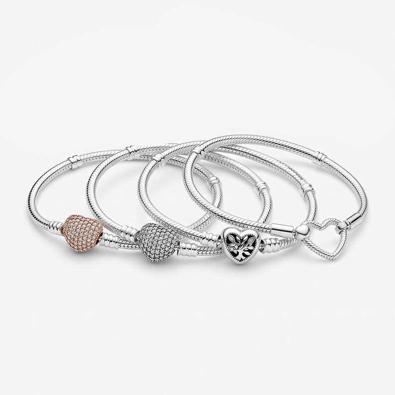 May include: Four silver-toned snake chain bracelets featuring heart-shaped charms. One charm is rose gold-toned with pav&eacute; stones, one is silver-toned with pav&eacute; stones, one is a silver heart with a tree motif, and one is a simple open heart clasp.