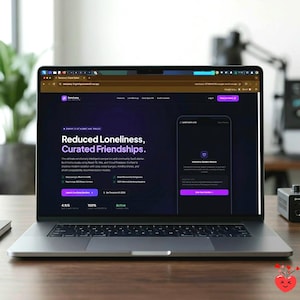 May include: A laptop displaying a website with the text "Reduced Loneliness, Curated Friendships." The website has a dark purple and white color scheme. The laptop is open on a wooden desk with a plant in the background.