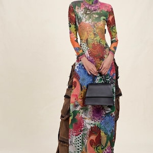 May include: A long-sleeved dress with a high neckline, featuring a colourful floral and koi carp print. The outfit includes brown trousers and a small, black handbag. The ensemble combines striking patterns and textures.