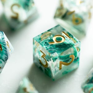 Könnte beinhalten: Nahaufnahme von mehreren Würfeln mit einem marmorierten türkis-weißen Design und goldfarbenen Zahlen. Die Würfel sind auf einer weißen Oberfläche verstreut, wobei einige fokussiert und andere unscharf sind.