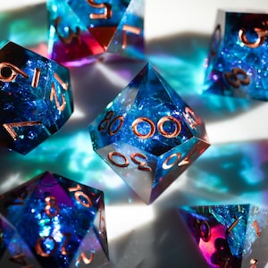 May include: A collection of polyhedral dice with a blue and purple iridescent interior and copper-colored numbering. The dice are arranged on a white surface, with light and shadow creating a dynamic effect. The dice are designed for tabletop gaming.