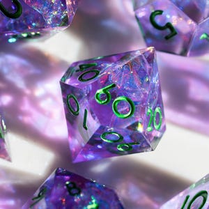 Peut inclure: Gros plan sur plusieurs dés polyédriques. Les dés sont transparents avec un effet pailleté violet et irisé. Les chiffres sont verts. Les dés sont pour les jeux de société.