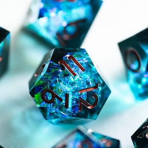 May include: Close-up of several polyhedral dice with a blue and green, ocean-like appearance. The dice have copper-colored numbers. The dice are for tabletop games like Dungeons and Dragons.