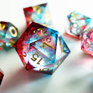 May include: A collection of polyhedral dice with a galaxy-like design. The dice are a mix of red, blue, and clear resin, with gold-colored numbers. The dice are in various shapes, including D4, D6, D8, D10, D12, and D20.