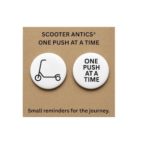 May include: Two white circular pin-back buttons attached to a tan card. One button features a black line drawing of a scooter, and the other displays the black text ONE PUSH AT A TIME. The card includes the text SCOOTER ANTICS ONE PUSH AT A TIME.