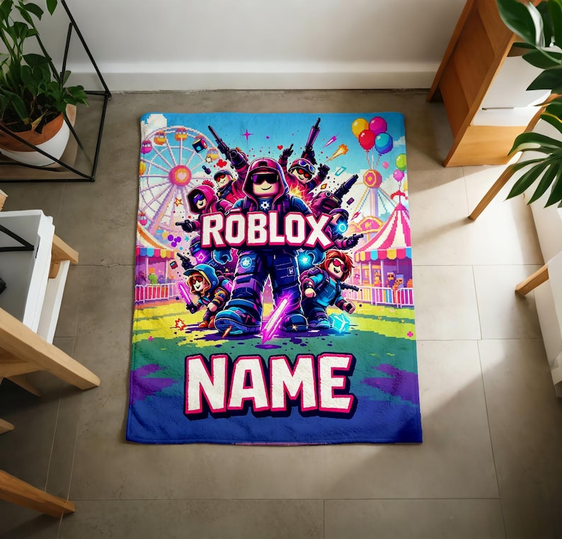 Puede incluir: Una manta rectangular azul con un dise&ntilde;o colorido de Roblox. La manta muestra el logotipo de Roblox y la palabra "NAME" en letras grandes. El dise&ntilde;o incluye personajes de dibujos animados, una noria y globos.