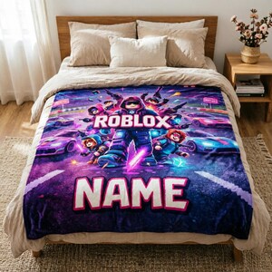 Puede incluir: Una vibrante y suave manta con un colorido dise&ntilde;o de Roblox. La manta muestra un personaje central de Roblox rodeado de otros personajes y coches de carreras, con las palabras "ROBLOX" y "NAME" en un lugar destacado.