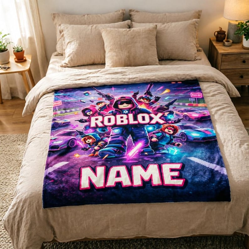 Puede incluir: Una manta rectangular de felpa con un dise&ntilde;o vibrante de Roblox. La manta muestra personajes de Roblox, coches de carreras y el logotipo de Roblox en una composici&oacute;n din&aacute;mica y colorida. La palabra "NAME" se muestra de forma destacada.