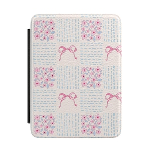 May include: A rectangular case with a floral and bow pattern. The case features a white background with light blue vertical lines and squares. Pink flowers and bows are evenly spaced across the surface. A black strap is on the left side.