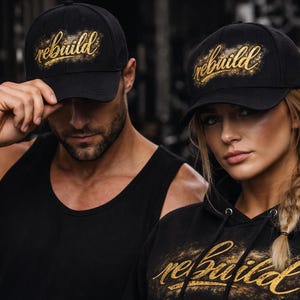 Peut inclure: Casquettes de baseball noires et un sweat à capuche noir avec le mot "rebuild" en script doré. Les casquettes sont portées par un homme et une femme, et le sweat à capuche est porté par la femme. L'arrière-plan est flou.