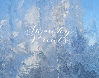 May include: A close-up of a frosted window pane with a blue sky visible through the ice crystals. The text "Swanky Prints" is written in white cursive lettering on the window.