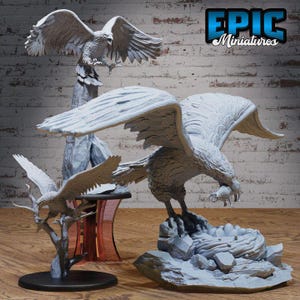 May include: A collection of gray eagle figurines in various poses. One eagle is perched atop a rocky nest with eggs, another is perched on a tree branch, and a third is perched on a stone column. The text "EPIC Miniatures" is visible.