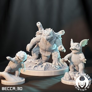 May include: Three white 3D-printed figurines of turtle-like creatures. The largest figure stands in the center, flanked by two smaller figures. The figures have detailed textures and are posed on circular bases. The text "BECCA_3D" is at the bottom left.
