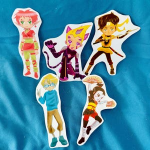May include: A collection of five die-cut stickers featuring anime-style characters. The characters are depicted in various action poses and outfits, with a range of colors including red, yellow, purple, and blue. The stickers are on a blue background.