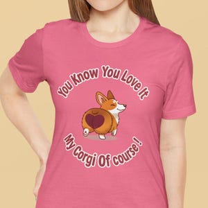 May include: A pink t-shirt featuring a cartoon corgi with a heart-shaped design on its rear. The shirt has the text "You Know You Love It, My Corgi Of Course!" in a circular pattern around the corgi illustration.