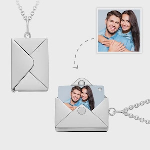 Peut inclure: Un collier pendentif argenté en forme d'enveloppe. Le pendentif s'ouvre pour révéler une petite photo. Le collier a une chaîne délicate. L'image montre un couple s'embrassant. Le pendentif est un accessoire unique et personnalisé.