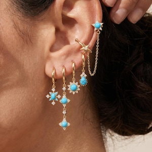 May include: A set of gold-toned earrings featuring bright turquoise stones and small clear crystals. The collection includes a star-shaped ear cuff connected by a delicate chain to a star stud, alongside three dangling hoop earrings with sunburst designs.
