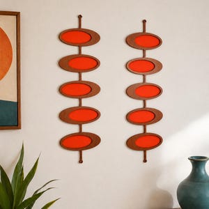 May include: Two vertical wall hangings, each featuring five stacked oval frames made of dark brown wood. Each frame contains a vibrant orange insert. The two pieces are mounted side-by-side on a plain wall, creating a symmetrical display.