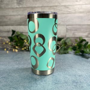 May include: A mint green stainless steel tumbler featuring a pattern of metallic silver circles and rounded square shapes. The cup has a clear lid and a metallic silver base, with a smooth finish that contrasts with the geometric silver design.