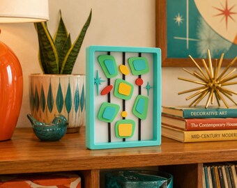 May include: A rectangular wall art piece with a bright turquoise frame featuring a white background, three vertical black lines, and layered geometric shapes in shades of lime green, yellow, turquoise, and red, accented by small turquoise starbursts.